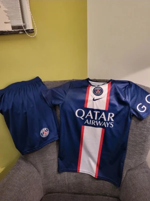 Nike Paris Saint-Germain PSG hemma Messi Set XS - Snyggt PSG matchställ i blått med Messi 30 på ryggen. Tröjan har vita och röda detaljer, Qatar Airways-tryck och PSG-logga framtill. Korta ärmar och tillhörande shorts med PSG-märke. Perfekt för fotbollsträning eller att bära som supporter.