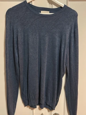 Mörkblå tunn stickad tröja  - En enkel och stilren mörkblå stickad tröja med rund halsringning och långa ärmar. Tröjan är tunn och har ribbade muddar vid ärmslut och nederkant. Perfekt att matcha med jeans eller kjol för en avslappnad look.
