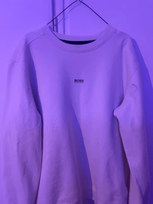 Hugo boss hoodie - Klassisk vit sweatshirt från BOSS med rund halsringning och diskret logga på bröstet. Tröjan har en avslappnad passform och är tillverkad i mjukt material, perfekt för en clean och stilren look.