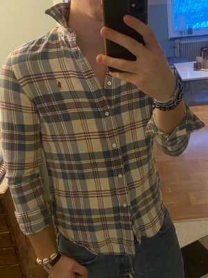 Rutig skjorta från Ralph Lauren - Klassisk rutig skjorta från Ralph Lauren i blått, vitt och rött. Skjortan har lång ärm, knappar framtill och den ikoniska broderade loggan på bröstet. Tillverkad i mjuk bomull. Perfekt för en avslappnad men ändå stilren look.