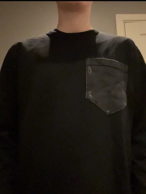 Svart sweatshirt från Dondup med jeansficka - Cool svart sweatshirt från Dondup med unik grå jeansficka på bröstet. Tröjan har rund halsringning och en snygg kontrast mellan det svarta tyget och den slitna jeansdetaljen. Perfekt för dig som vill sticka ut med en streetinspirerad look. Aldrig använd