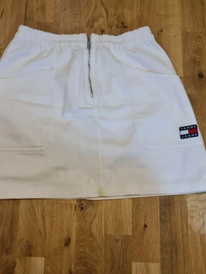 Vit kortkjol från Tommy Jeans - En vit Tommy Jeans kjol, den är dock lite smutsig som ni ser på bilderna fast de är inget äckligt! Utan jag fick på mig lite orange juice som inte gick att ta bort annars är de jätte bra och jättefint också! För mer frågar skriv gärna till mig!!🤍🤍