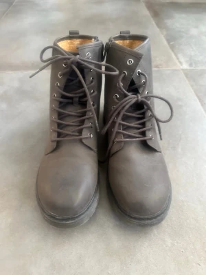 Bruna snörade kängor från ZARA - Snygga bruna kängor från ZARA med snörning framtill och robust sula. Tillverkade i ett matt material som ger en stilren look. Kängorna har dragkedja på insidan för enkel på- och avtagning samt metallöljetter för snörena.  Nya oanvända