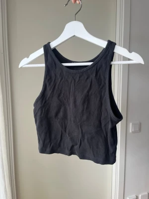 Svart ribbad topp från Zara  - Snygg svart croppad linnetopp med ribbad struktur. Toppen är ärmlös och har en klassisk rund halsringning. Perfekt att styla med jeans eller kjol för en trendig look. Storlek L men passar mer S-M 
