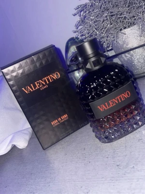 Valentino Uomo Born In Roma Coral Famtasy parfym 100 ml - Valentino Uomo Born In Roma Coral Fantasy parfym med en lyxig, mörk glasflaska i diamantmönster och svart kork. Flaskan har en gradient från svart till rödbrun och etiketten är svart med orange text. Kommer i matchande svart kartong med samma design.