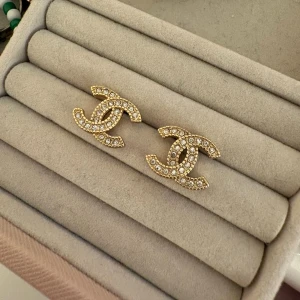 Guldiga Chanel örhängen med pärlor - Snygga örhängen i guldfärgad metall med ikoniska CC-loggan täckt av små glittrande pärlor. Perfekta för dig som vill ha en lyxig och trendig accessoar som sticker ut. Klassisk design som passar till många olika stilar.🥰