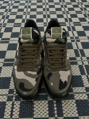 Valentino Garavani camo sneakers - Snygga sneakers från Valentino Garavani med camomönster i grönt, svart och beige. Skorna har låga skaft, gröna snören och detaljer i mocka och mesh. Perfekta för dig som vill sticka ut med en exklusiv touch.