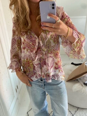 Blommig volangblus från Zara  - Superfin blus i ett rosa/lila/grönt blommigt mönster med volangdetaljer och knyt framtill. . Blusen har långa och vida ärmar och ett luftigt tunt, lätt transparent tyg, perfekt för sommaren.