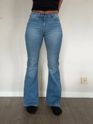 Ljusblå bootcut jeans med hög midja - Ljusblå bootcut jeans med hög midja och klassisk femficksmodell. Jeansen har utsvängda ben och stängs med dragkedja och knapp. Perfekta för dig som gillar retrovibbar och en bekväm passform. Storlek: W25 L31