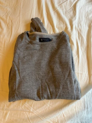 Grå stickad tröja från Riley - Snygg grå stickad tröja från Riley med rund halsringning. Tröjan är enkel och stilren, perfekt för lager på lager och har en mjuk känsla. Passar dig som gillar klassisk och tidlös design. Storlek M men passar S