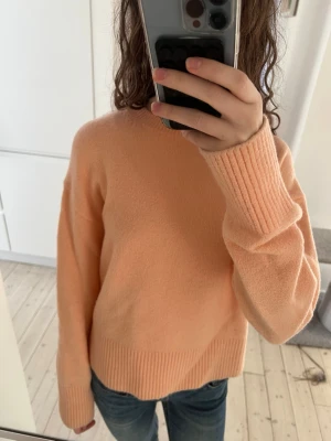 Persikofärgad stickad tröja - Mysig persikofärgad stickad tröja med rund hals och ribbade muddar vid ärmslut och nederkant. Tröjan har en avslappnad passform och är perfekt för lager på lager. Materialet ser mjukt och skönt ut, perfekt för kyligare dagar. Orginal priset är 800 kr 🥰 