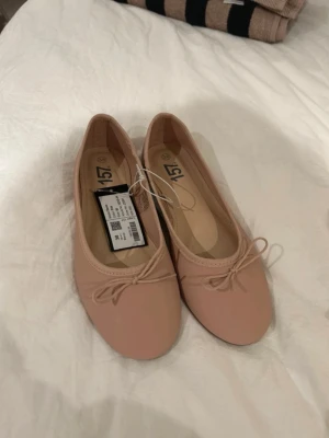 Rosa ballerinaskor med rosett - Säljer ett par stilrena rosa ballerinaskor med en rosettdetalj framtill. Aldrig använda 