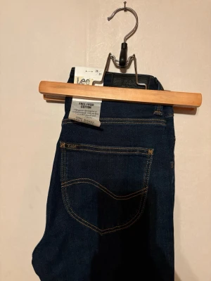 Mörkblå Lee jeans med smala ben - Snygga mörkblå jeans från Lee med klassisk femficksdesign, raka ben och hög midja. Jeansen har kontrastsömmar och en Lee-logga på bakfickan. Perfekta till din vardagsstil!