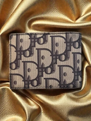 Gold monogram plånbok i canvas - Snygg plånbok från D med klassiskt blått monogrammönster på beige canvas. Insidan är mörkblå med flera kortfack och en myntficka med knappstängning. Perfekt accessoar för dig som gillar lyxiga detaljer och tidlös design.