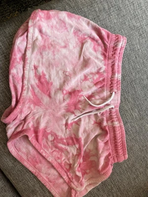 Rosa tie-dye shorts med snörning - Säljer ett par mjuka och sköna shorts i rosa och vitt tie-dye mönster. Shortsen har elastisk midja med vit snörning och avslappnad passform. Perfekta för sommardagar eller att chilla hemma i.