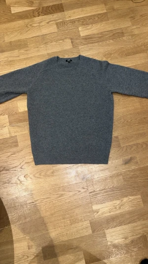 Grå stickad tröja från Uniqlo - Mysig grå stickad tröja från Uniqlo i enkel och klassisk design. Tröjan har rund halsringning, långa ärmar och ribbstickade muddar vid ärmslut och nederkant. 