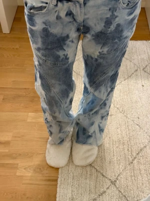 Blå tie-dye baggy jeans - Säljer ett par blå tie-dye jeans med baggy passform och raka ben. Jeansen har coola sömdetaljer och klassiska fickor både fram och bak. Perfekta för dig som gillar en avslappnad och trendig stil.