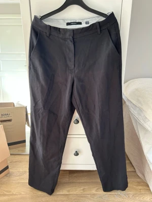 Svarta kostymbyxor från Veromoda  - Stilrena svarta kostymbyxor från VeroModa med raka ben och pressveck. Byxorna har två sidofickor fram och två passpoalfickor bak. Klassisk midja med hällor för skärp. Perfekta till en dressad look och otroligt bekväma!