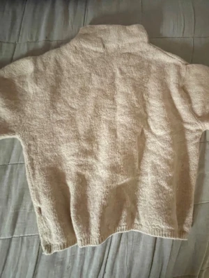 Beige stickad polotröja - Mysig beige stickad polotröja med hög krage och lång ärm. Tröjan har en enkel och avslappnad passform, perfekt för lager på lager. Materialet känns mjukt och värmande, vilket gör den idealisk för kyligare dagar.
