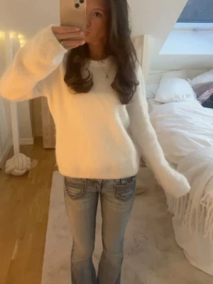 Vit fluffig stickad tröja - Mysig vit stickad tröja med fluffig textur och rund hals. Tröjan har långa ärmar och en avslappnad passform, perfekt för kalla dagar. Passar till jeans eller kjol för en enkel och trendig look.