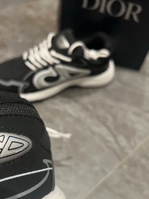 Zara skor - Säljer ett par svarta sneakers med vita och silverfärgade detaljer. Skorna har en chunky sula, vita skosnören och en stor reflekterande logga på sidan. Materialmix av mesh och läder ger en modern och sportig look.