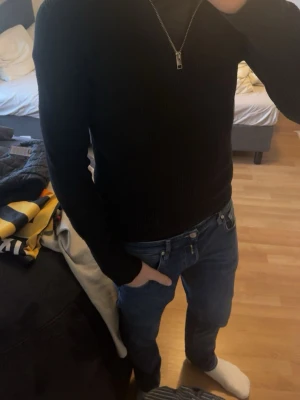 Svart stickad tröja med halvzip - Säljer en svart stickad tröja från Jack & Jones  med halvzip och hög krage. Tröjan är ribbstickad och har långa ärmar. Perfekt för lager på lager och enkel att matcha med jeans eller chinos. M kan passa S också!