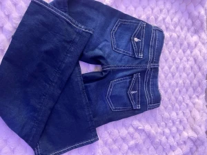 Mörkblå bootcut jeans med kontrastsömmar - Säljer ett par mörkblå bootcut jeans med vita kontrastsömmar och snygga fickdetaljer bak. Jeansen har klassisk femficksdesign och är perfekta för dig som gillar en tidlös men trendig look. Materialet känns mjukt och följsamt.