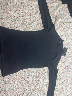 Svart långärmad träningströja UA - Svart långärmad träningströja från Under Armour med tight passform och ColdGear-teknologi som håller dig varm under kalla träningspass. Perfekt för löpning eller gym. Diskret UA-logga vid halsen och mjukt, stretchigt material.