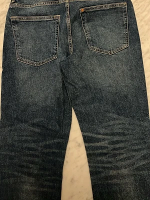 Mörkblå raka jeans - Klassiska mörkblå jeans med raka ben och femficksmodell. Jeansen har slitningar och tvättade detaljer för en avslappnad look. Tillverkade i robust denim med kontrastsömmar och läderpatch bak. W29 L32