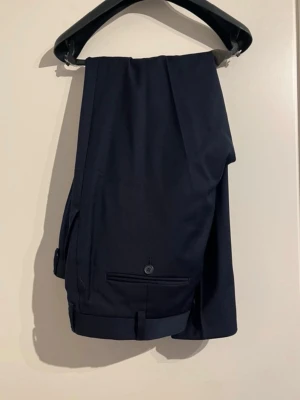 Mörkblå kostymbyxor herr - Snygga mörkblå kostymbyxor med klassisk rak passform. Byxorna har diskreta bakfickor med knapp och stilren design. Perfekta till skjorta eller kavaj för en clean look. Finns kavaj som matchar (gör gärna bundle). Skriv vid frågor och pris kan diskuteras!