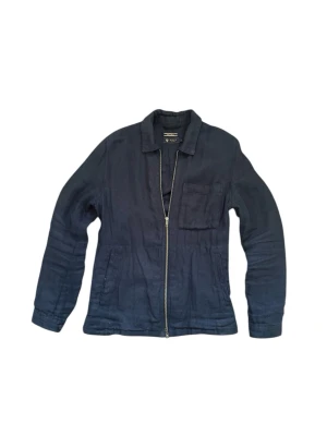 Linne Overshirt  - Stilren mörkblå overshirt  i ett lätt linnematerial. Modellen har klassisk krage, dragkedja framtill, en bröstficka och två sidofickor. Perfekt lager-på-lager-plagg med avslappnad passform och lång ärm.