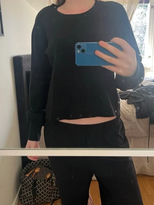Svart långärmad tröja med rund hals - En enkel svart långärmad tröja med rund hals och rak passform. Tröjan är mjuk och har ribbade muddar vid ärmslut. Perfekt för att matcha med jeans eller mjukisbyxor. Materialet ser ut att vara bomull eller en bomullsblandning.