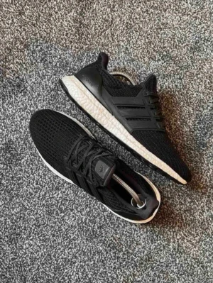 Adidas Ultra Boost svarta sneakers - Svarta Adidas Ultra Boost sneakers med stickad mesh-överdel och vit Boost-sula. Skorna har klassiska tre ränder på sidan och en låg profil. Perfekta för dig som vill ha både stil och komfort. Materialet är lätt och andas, vilket gör dem grymma för vardagsbruk.