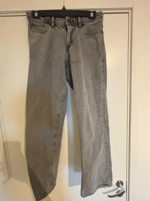 Grå raka jeans med hög midja Jack & Jones - Ett par grå jeans med rak passform och hög midja. Jeansen har klassiska fem fickor, bälteshällor och dragkedjegylf. Materialet är denim i bomull och färgen är tvättad grå, vilket ger en cool vintagekänsla.