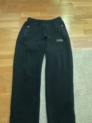 Svarta AMG Petronas mjukisbyxor - Säljer ett par svarta mjukisbyxor från Mercedes AMG Petronas Formula One Team. Byxorna har dragsko i midjan, raka ben och två fickor fram. Materialet är mjukt och bekvämt, perfekt för chill dagar. Snygg logga på ena benet för dig som gillar racing.