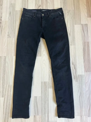 Svarta  jeans från Replay - Snygga svarta Slim fit jeans från Replay med klassisk femficksmodell och diskret logga vid fickan. Jeansen har smal passform och är tillverkade i ett stretchigt material som sitter bekvämt. Perfekta för en trendig och avslappnad stil.