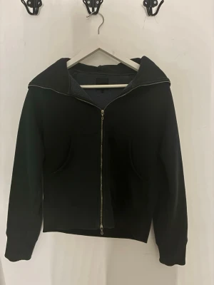 Svart zip hoodie från acne  - Säljer en svart hoodie från Acne Studios med dragkedja framtill och stor huva. Hoodien har två fickor på framsidan och ribbade muddar vid ärmar och midja. Hoodien har en lite kortare modell.