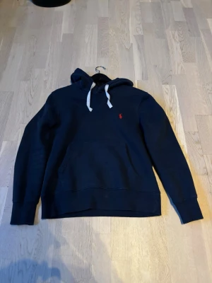 Mörkblå hoodie från Polo Ralph Lauren - Mörkblå hoodie från Polo Ralph Lauren med vit dragsko och klassisk röd logga på bröstet. Hoodien har en stor känguruficka framtill och är tillverkad i mjukt bomullsmaterial. Perfekt för en avslappnad och cool look. Pris går att diskutera🤗