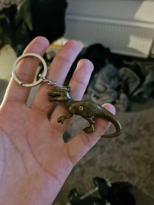 Nyckelring med dinosaurie i metall - Cool nyckelring med en dinosauriefigur i bronsfärgad metall. Dinosaurien har detaljerade former och sitter fast i en klassisk metallkedja med ring. Perfekt accessoar för dig som gillar unika detaljer och dinosaurier.