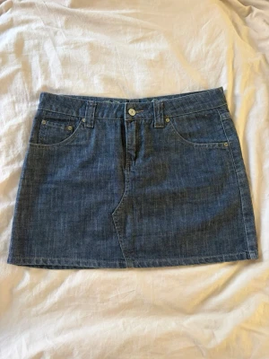 Blå jeanskjol med fickor - Säljer en klassisk blå jeanskjol med två framfickor och två bakfickor. Kjolen har hällor för bälte och stängs med knapp och dragkedja. Perfekt för dig som gillar en enkel och tidlös look. Midjemåttet är 76cm🙌🏻