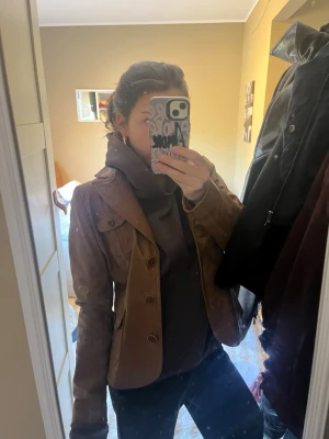 Brun skinnjacka från BlendShe - Snygg brun skinnjacka/läder från BlendShe med klassisk krage och knäppning framtill. Jackan har dekorativa fickor på bröstet och en figurnära passform som ger en cool och tidlös look. Perfekt för dig som vill ha en stilren jacka i äkta skinn.