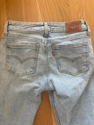 Ljusblå Levi's jeans med raka ben - Säljer ett par klassiska ljusblå Levi's jeans med raka ben och femficksmodell. Jeansen har den ikoniska röda Levi's-lappen på bakfickan och patch i läder bak i midjan. Perfekta för en avslappnad och trendig look. Nyskick low waisted