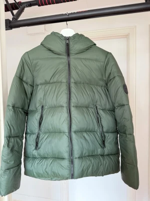 Grön pufferjacka med luva - Snygg grön pufferjacka med luva och dragkedja framtill. Endast använd 2 gånger