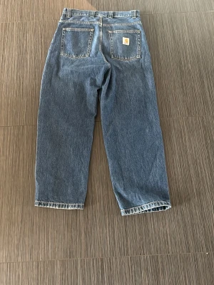 Blå raka jeans från Carhartt - Säljer ett par klassiska blå raka jeans från Carhartt. Jeansen har fem fickor och tydliga sömmar. Baktill finns Carhartt-loggan på ena fickan. Tillverkade i slitstark denim, perfekta för en avslappnad streetwear-look.