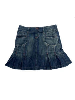 Blå jeanskjol med fickor och veck - Blå jeanskjol med två framfickor och snygga veckdetaljer runt om vilket gör att den böljar ut. Kjolen har röda sömmar som kontrast och klassisk jeansknapp och kort dragkedja i midjan. Medellånga. Storlek 40. Stradavius españa, 100% bomull.