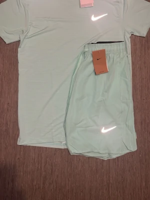 Nike Miller set - Säljer ett ljusgrönt träningsset från Nike med matchande t-shirt och shorts. Båda plaggen har den klassiska Nike-loggan framtill och är tillverkade i ett lätt, syntetiskt material som andas. Perfekt för dig som vill ha ett stilrent och sportigt set till träningen.STORLEKSINFO: Lappen säger XL (Kina), men motsvarar en EU Medium (M). • Bröst: 102–108 cm. • Midja: 95–101 cm.