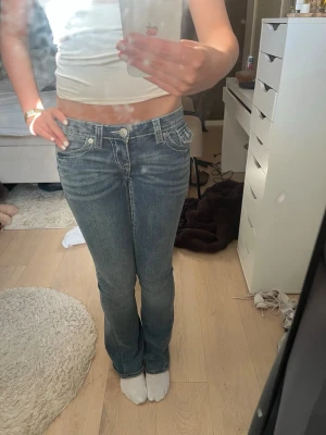 Blå bootcut jeans True Religion - Säljer ett par blå bootcut jeans från True Religion med vita kontrastsömmar och stora fickor bak med broderade detaljer. Jeansen har låg midja och klassisk femficksdesign.