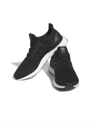 Svarta Adidas Ultraboost sneakers - Snygga svarta Adidas Ultraboost sneakers med stickad ovandel och vita Boost-sulor. Skorna har klassiska tre ränder på sidan och en sportig, modern look. Perfekta för dig som gillar streetwear och komfort. Materialet är mesh och syntet.