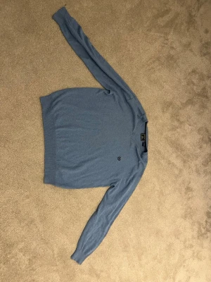 Blå stickad tröja från Ralph Lauren Chaps - Mysig blå stickad tröja från Chaps med V-ringning och diskret logga på bröstet. Tillverkad i en mjuk blandning av bomull och kashmir som känns lyxig och bekväm. Perfekt för lager på lager och enkel att matcha med jeans eller kjol.