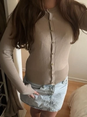 Beige ribbad kofta med knappar - Snygg beige kofta med ribbade detaljer och långa ärmar. Koftan har en figurnära passform och stängs med små, ljusa knappar framtill. Perfekt att styla med jeans eller kjol för en clean look.